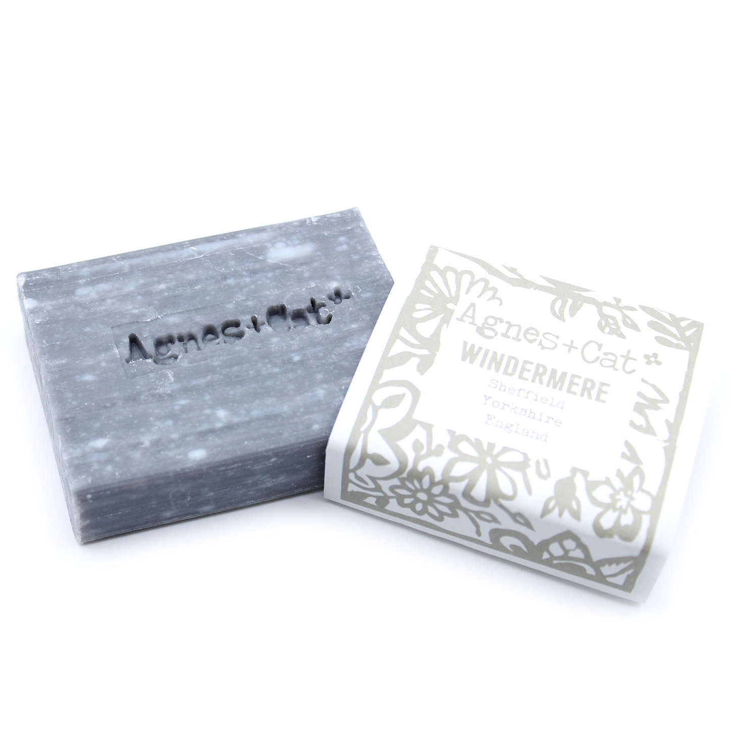 Jabón Artesanal Agnes+Cat Windermere 140g, natural y aromático, mostrando la pastilla de jabón saliendo de su envoltorio, ideal para una experiencia de limpieza relajante.