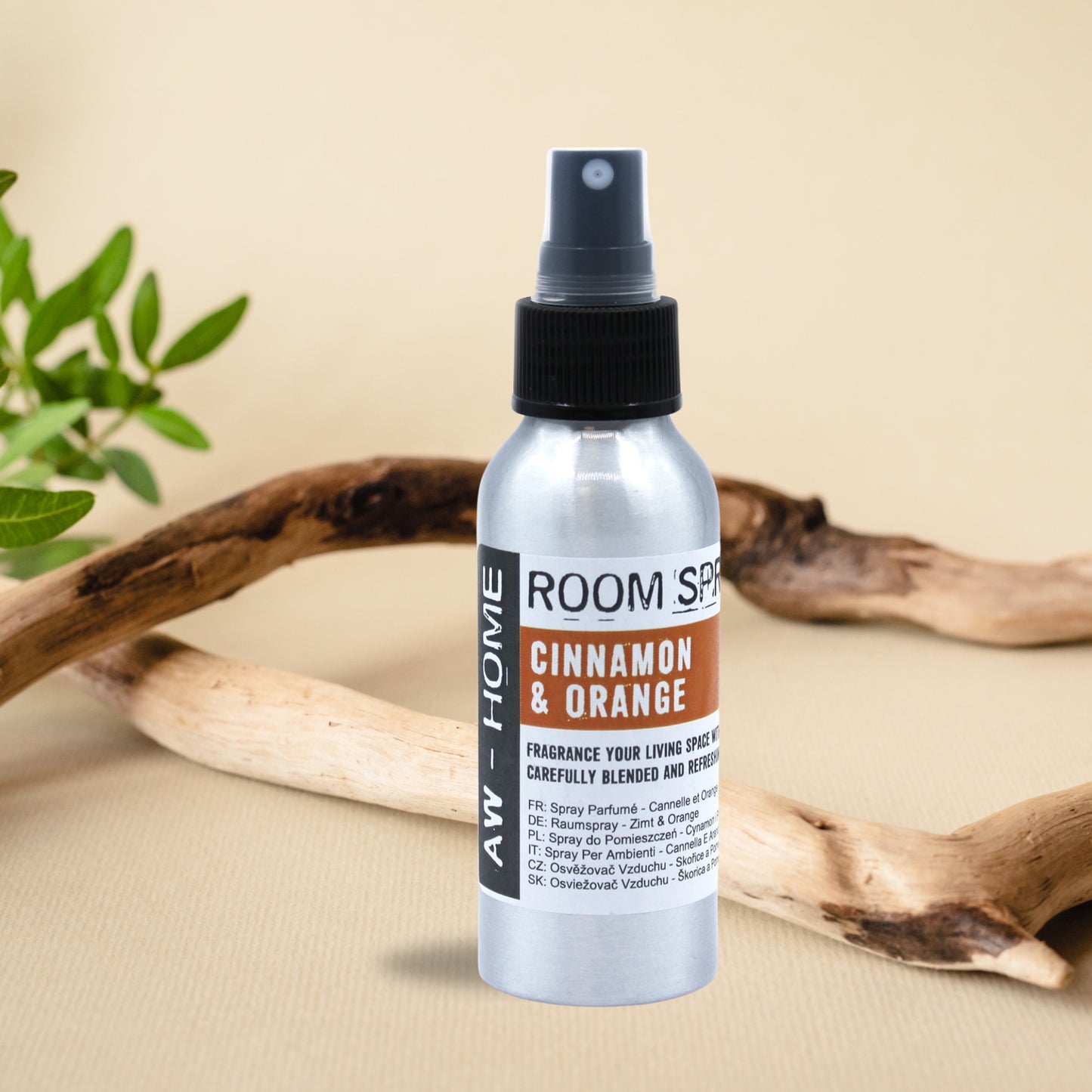 Spray ambiental de canela y naranja de 100 ml en un frasco de aluminio, colocado sobre una mesa con ramas decorativas.